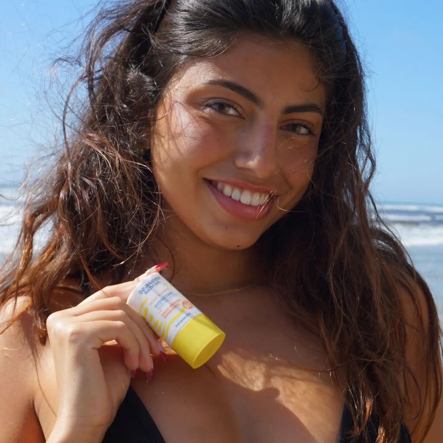 Girl Holding Seaweed Bath Co Hydrating Serun Stick SPF 50 on the beach