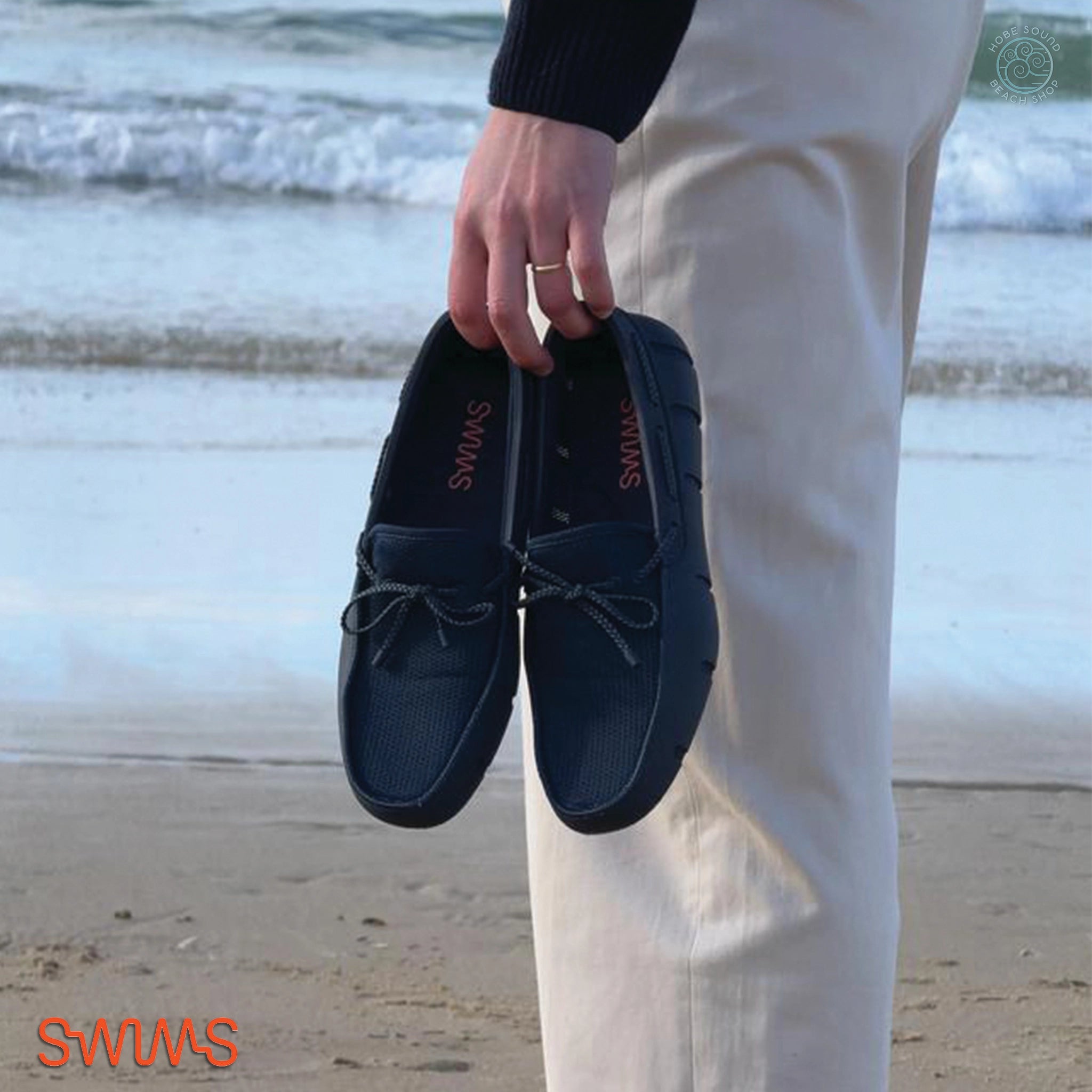 Person holding Swims Braided Lace navy loafers on a beach.
